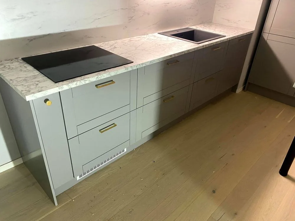 Kök med ljusgrå ramluckor, mässingsgrepp och marmorerad bänkskiva